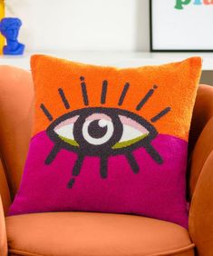 an orange chair with a pink pillow on it and a colorful eye cushion in the middle