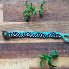 a blue and black beaded wristband on a wooden table next to green leaves