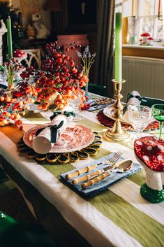 a table set for christmas dinner with plates and silverware on it, candlesticks in the background