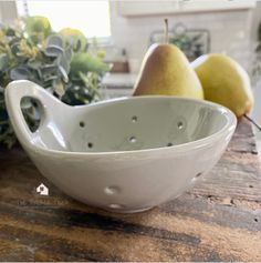 a white bowl sitting on top of a wooden table next to pears and greenery