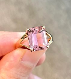 a person holding a pink ring with an emerald cut stone in it's center