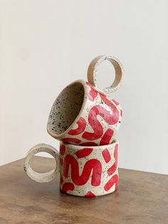 two ceramic cups sitting on top of a wooden table next to each other, one with red and white designs