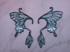 two metal wall hangings on a white marble counter with blue and green designs in the shape of wings