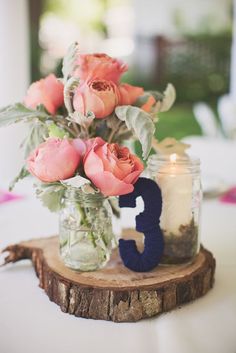 flowers in mason jars on a table with a candle and number 3 sign next to it