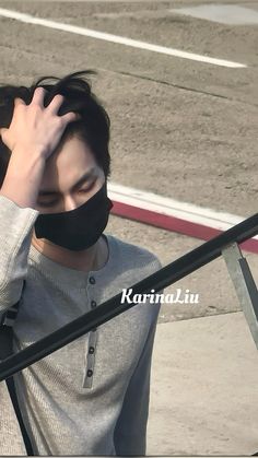 a young man wearing a black mask and holding his hand up to his face while standing on an airport tarmac