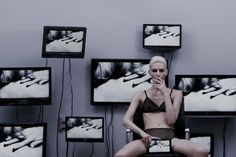 a woman sitting on a chair in front of televisions and holding a cell phone