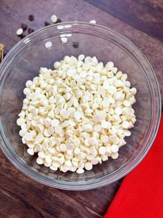 a glass bowl filled with white beans on top of a wooden table next to a red napkin