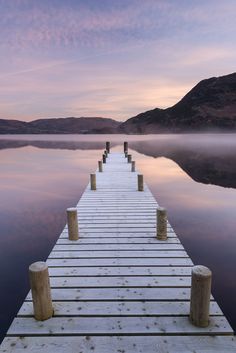 a dock that is in the middle of some water with mountains in the background and clouds in the sky