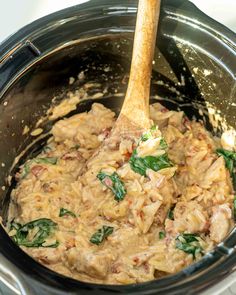 a wooden spoon in a slow cooker filled with meat and spinach mixtures