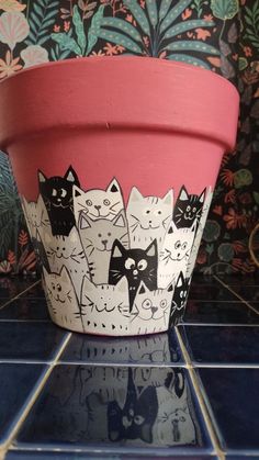 a pot with cats painted on it sitting on a tile floor next to a wall