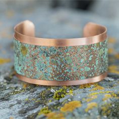 a copper cuff with green and brown speckles is sitting on top of a rock