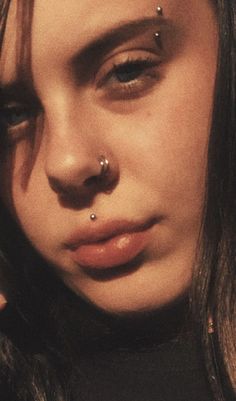 a close up of a person with piercings on her nose and nose ring in their left hand