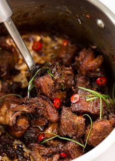 a pot filled with meat and garnish on top of a table next to a spoon