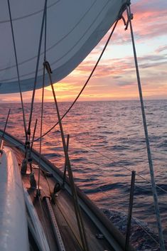 the sun is setting over the ocean on a sailboat