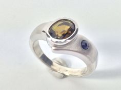 "Hi everyone, just wanted to let you know we are open and shipping daily. Beautifully crafted \"one of a kind\" contemporary Sterling Silver ring with genuine chrome tourmaline and Sapphire stones. The silver ring is finished with Rhodium so it will not tarnish. The gemstone used in this ring has been hand picked on a recent trip to Bangkok and is of a quality usually reserved for fine jewelry so you will almost never find such nice stones set in sterling silver! Weight 8 Grams This fine jewelry Modern Silver Sapphire Ring With Accent Stones, Modern Silver Sapphire Ring With Tension Setting, Modern Silver Sapphire Ring, Modern Silver Oval Sapphire Ring, Modern Silver Sapphire Ring Oval Shaped, Modern White Gold Sapphire Ring, Modern Sapphire Ring With Polished Finish, Sapphire Silver Ring, Chrome Tourmaline