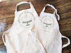 two white aprons sitting on top of a wooden table