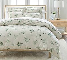 a bed with white sheets and green plants on it in a room next to a window