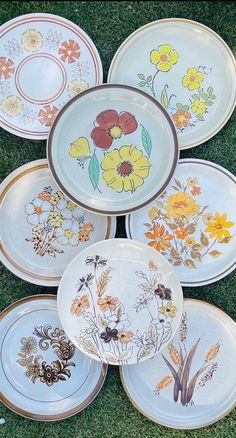 several plates with flowers painted on them are laying in the grass and there is no image here to provide a caption for