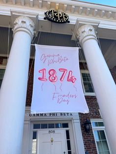 a large sign hanging from the side of a building next to two white pillars and a clock