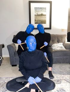 three people sitting on the floor with blue paint on their faces and hands, holding sticks