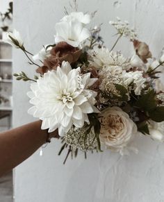 a bouquet of flowers is being held up against a wall by someone's hand