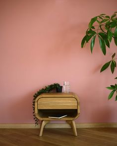 a small wooden table sitting next to a pink wall