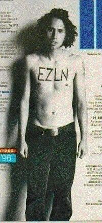 a man with no shirt on standing in front of a newspaper article that says ezln