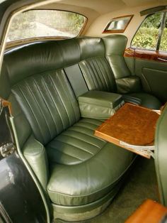 the interior of an old car with green leather seats and wood table in front of it