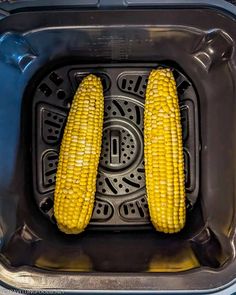 two corn on the cob being cooked in an air fryer with no lid