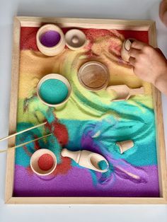 a child playing with an art project made out of colored sand and wooden spoons