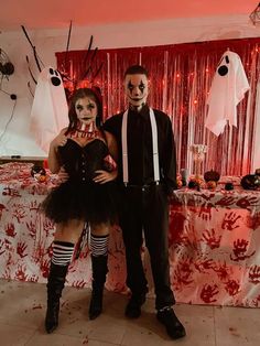 a man and woman dressed up in costumes standing next to a table with halloween decorations