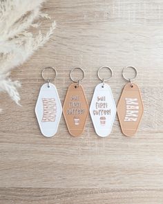 three leather key chains with words on them sitting on a wooden table next to feathers