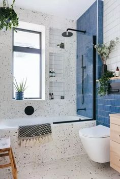 a white toilet sitting next to a bath tub under a window in a blue tiled bathroom