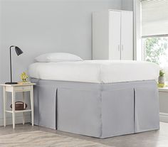 a bed with a white headboard and grey bedskirt next to a window