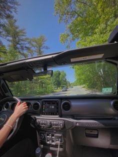 a woman driving a car on a road with trees in the background