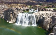 the waterfall is surrounded by large rocks and green water, with a rainbow in the middle