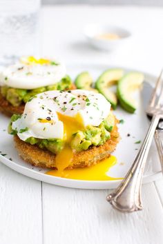 an egg and avocado sandwich on a white plate with silver utensils