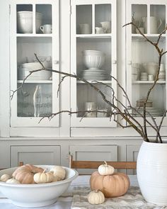 a white china cabinet filled with dishes and pumpkins on top of a wooden table