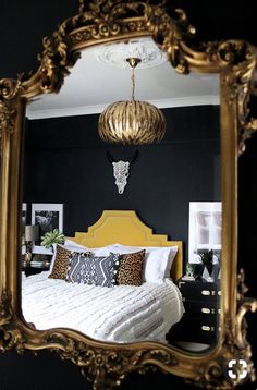 a bedroom with a large gold mirror hanging above it's bed and black walls