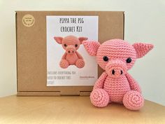 a pink crocheted pig sitting next to a cardboard box