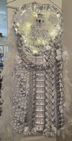 a white teddy bear in a dress made out of silver and white feathers hanging from a hook