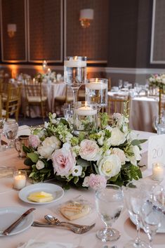 the centerpieces on this table are filled with white and pink flowers, greenery, and candles