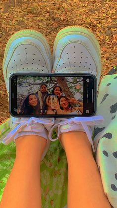 someone taking a selfie with their cell phone while sitting on the ground in front of some leaves