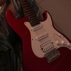 a red electric guitar sitting on top of a person's lap next to a wall