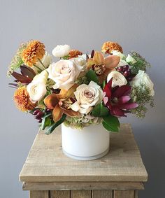 a white vase filled with lots of flowers on top of a wooden table next to a gray wall