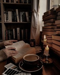 a person is reading a book in front of a cup of coffee and some books