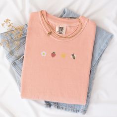 Welcome the sunny days with our Sunkissed Strawberry and Bee Embroidered T-Shirt! Made from 100% cotton Soft Comfort Colors, this shirt is both stylish and comfortable, perfect for your summer adventures.Features:Material: 100% cotton Soft Comfort ColorsSizes: S, M, L, XL, 2XL (refer to size chart in images)Colors Available: Banana, Bay, Blossom, Chalky Mint, Chambray, Ivory, Orchid, Peachy, Violet (Note: Colors may vary slightly due to monitor settings)Design: Summer-inspired embroidery featuring a daisy, strawberry, sun, and bee on the center chestCare Instructions: Machine wash cold, tumble dry lowThis Sunlissed Strawberry and Bee Embroidered T-Shirt is a delightful addition to your wardrobe, bringing a touch of sunshine wherever you go. Perfect for picnics, beach days, or casual outing Bee T Shirt, Summer Apparel, Bee Embroidery, Summer Styles, Sweet Summer, Summer Adventures, Embroidered Tshirt, Beach Days, Beach Day