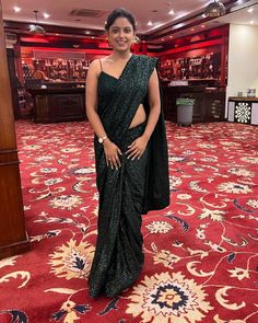 a woman in a black sari standing on a red carpeted area with an ornate pattern