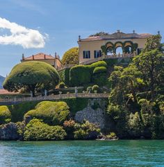 an island with trees and bushes on the top is surrounded by mountains, water and blue sky