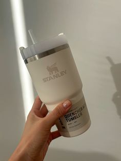 a hand holding a starbucks cup in front of a wall with the name stanley on it